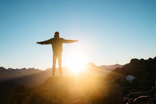 Sunset man on mountain hill hands extended blue sky